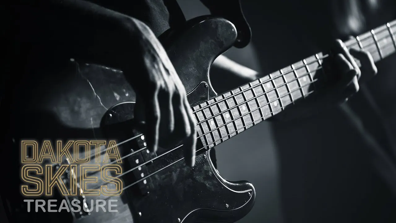 Close-up of hands playing an electric bass guitar in black and white with the words 'Dakota Skies Treasure' overlaid.