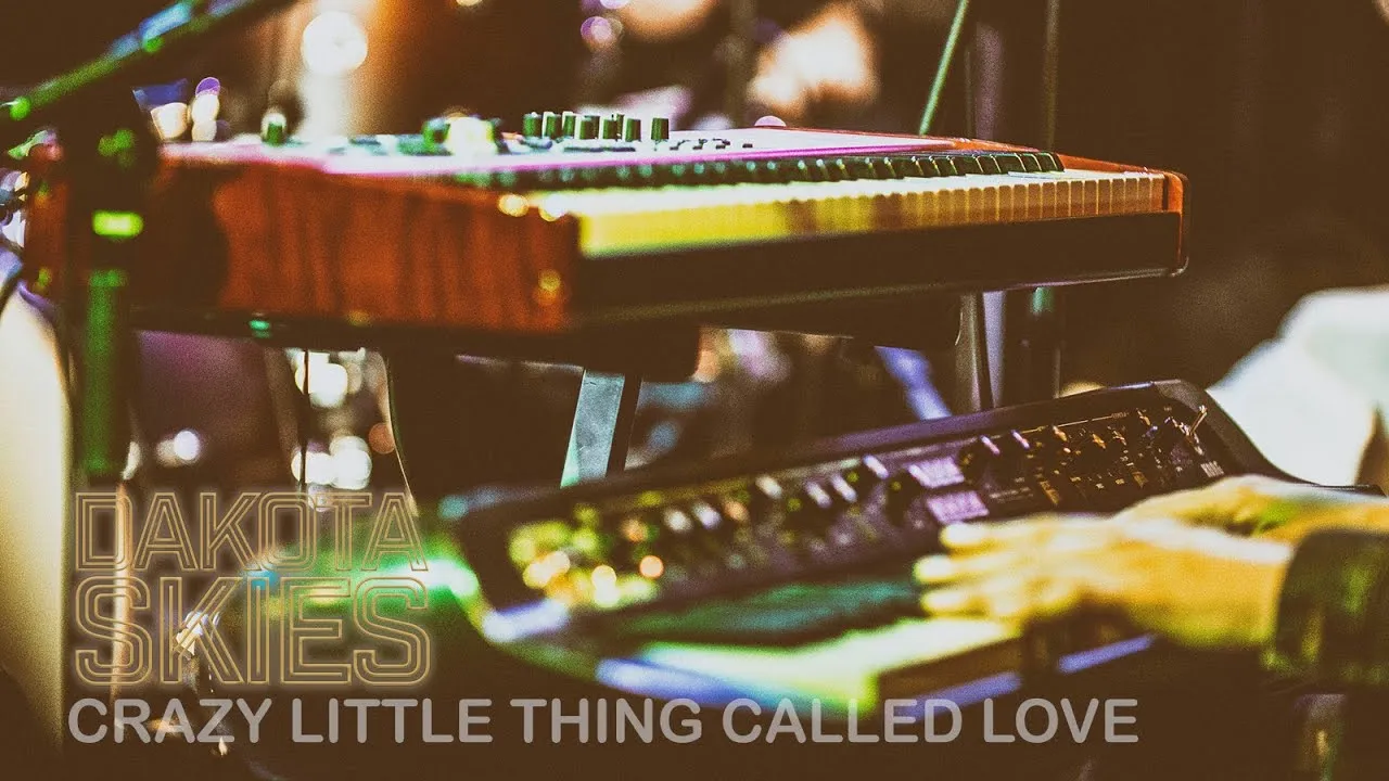 Close-up of musician playing two keyboards with overlay text saying Dakota Skies Crazy Little Thing Called Love.